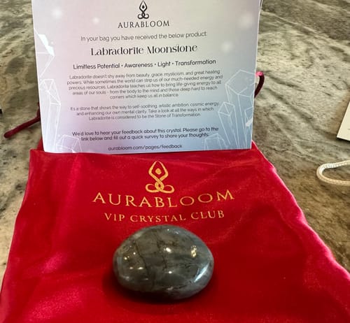 Customer's polished labradorite moonstone crystal from the AuraBloom box, with a red branded pouch and information card.