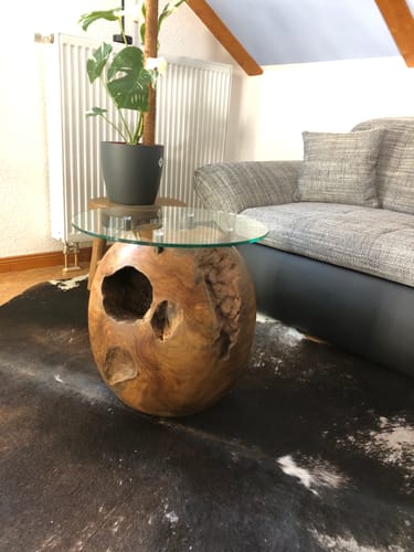 Kundenfoto des Teak Kugel Beistelltischs ROCCO mit Glasplatte, platziert neben einem Sofa im Wohnzimmer.
