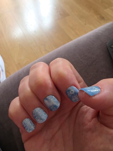 A customer's hand showing nails with light blue Holy Gels in a sun and cloud design.