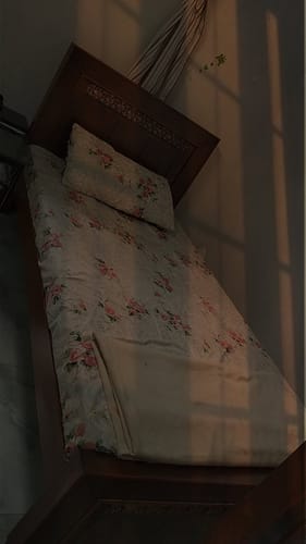 Customer's Zigma single bedsheet set with a floral pattern on a wooden bed in a warmly lit room.