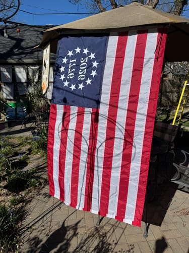Customer's Betsy Ross flag from the Patriotic Decor Kit hanging vertically on a sunny outdoor patio.