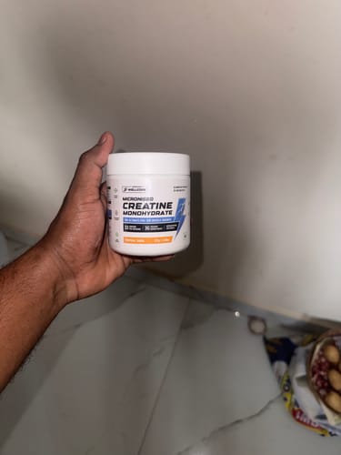 A customer's hand holding the white tub of Wellcore Pure Micronised Creatine Monohydrate indoors.