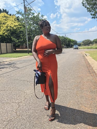 A reviewer stands on a street wearing the vibrant orange Off Shoulder Side Slit Dress.