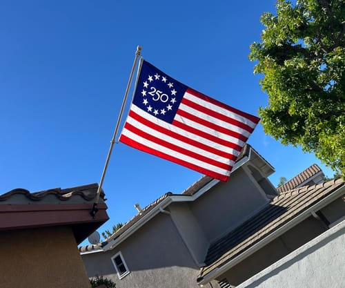 Customer's America 250 Betsy Ross Flag waving from a flagpole on their home against a clear blue sky.