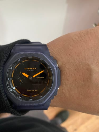 Primer plano del reloj Casio G-Shock Casioak en la muñeca de un cliente, con caja translúcida y manecillas naranjas.