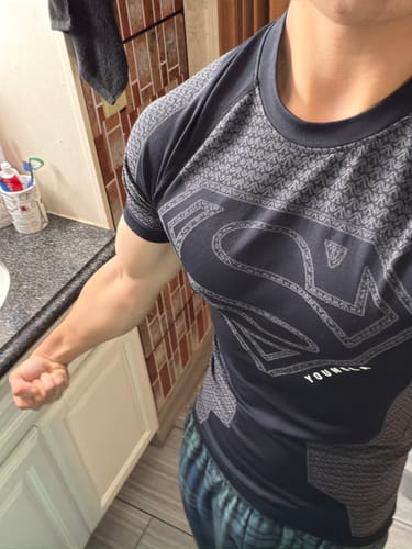 Customer shows off the athletic fit of the black Superman Compression Tee while flexing their arm.