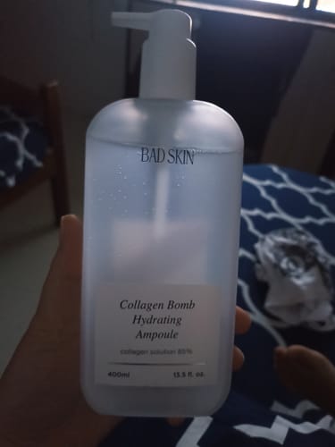 Reviewer holding the large, clear bottle of Bad Skin Collagen Bomb Hydrating Ampoule.
