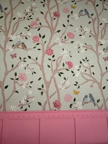 Close-up of a customer's Lockie Wallpaper with a charming bird and flower pattern installed above pink wainscoting.