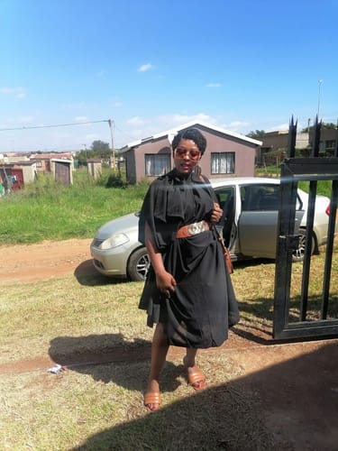 Reviewer outdoors in the black Majestic Elegant Cape-Sleeve Dress, styled with a wide brown belt.