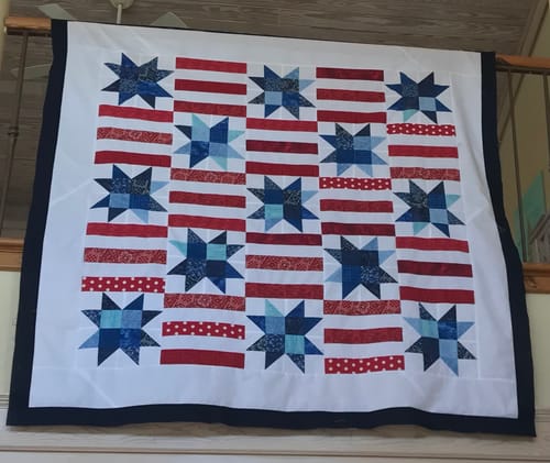 Customer's completed Red, White, and Cute quilt with a patriotic star pattern hanging over a railing.