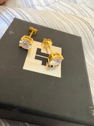 Customer's gold VVS Moissanite Solitaire Stud Earrings with screw backs resting on their product box.