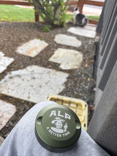 Customer's green ALP nicotine pouch tin resting on their lap in a backyard setting.