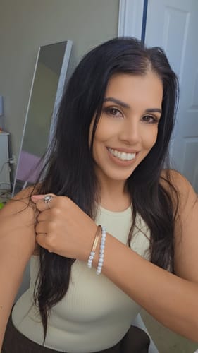A smiling reviewer wearing the white stone beaded bracelet on her wrist, stacked with a gold bangle.