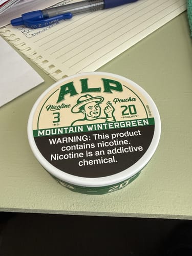 Customer's can of 3mg ALP Mountain Wintergreen Nicotine Pouches sitting on a desk next to a notepad.