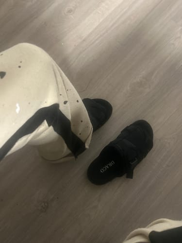 Customer's overhead view of their black Original Dracoslides on a wooden floor, with one on foot and the other off.