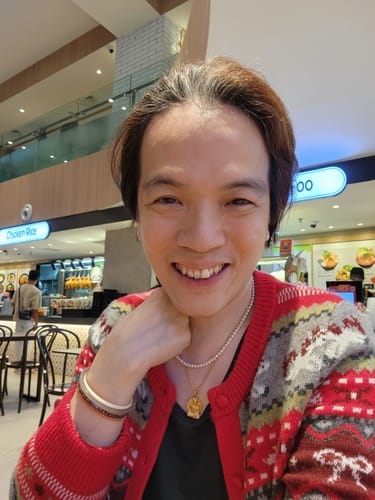 Customer wearing the patterned red and grey knitted cardigan, smiling at the camera in a food court.