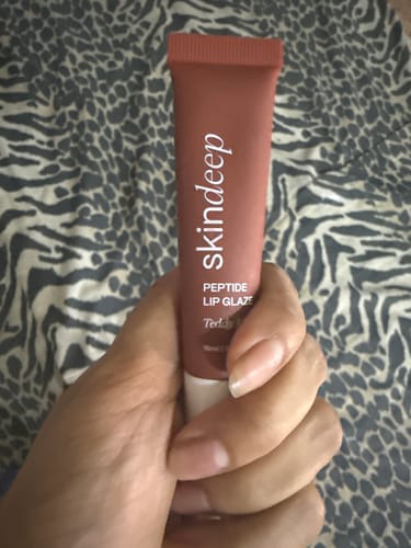Customer holding the dusty rose tube of skindeep Peptide Lip Glaze against an animal print background.