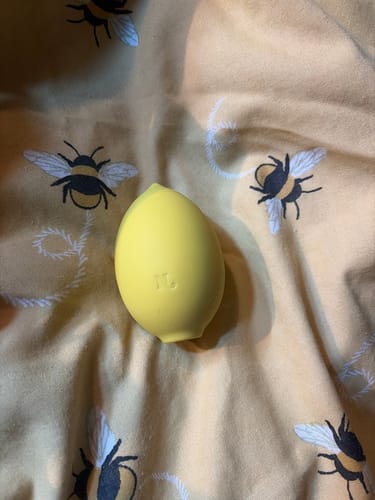 Customer's yellow Lem Clitoral Massager lying on a fabric with a bee print.