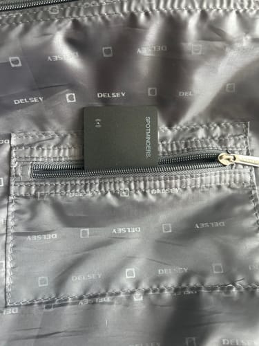 Customer's black SPOTMINDERS Tracking Card placed in the zippered pocket of a gray suitcase lining.