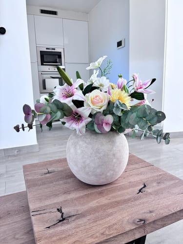 Recensent toont de grote, beige Terra vaas met een vol boeket bloemen op een houten tafel.