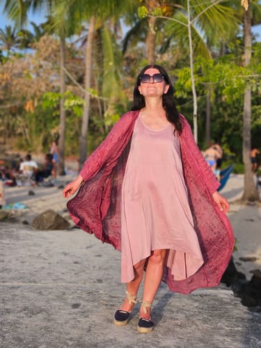 Reviewer on a beach holding open the flowy antique ruby silk jacket over a pink dress.