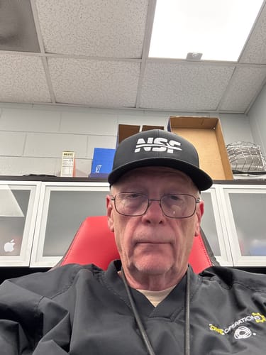 A reviewer wearing the black NSF Snapback Trucker Hat with a white logo in an office.