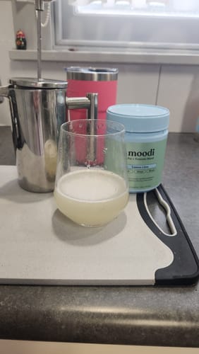 Customer's glass of frothy Lemon Lime drink next to the product container on a kitchen counter.