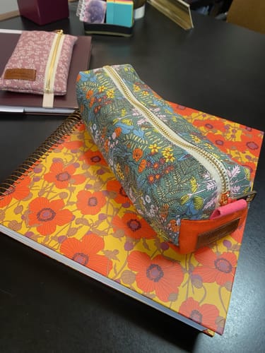 Customer's floral Dreamfern Pen Pouch sitting on a bright patterned notebook on a desk.