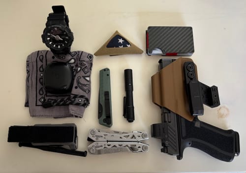 Reviewer's tan T1-M holster holding a pistol, laid out flat with other everyday carry items.
