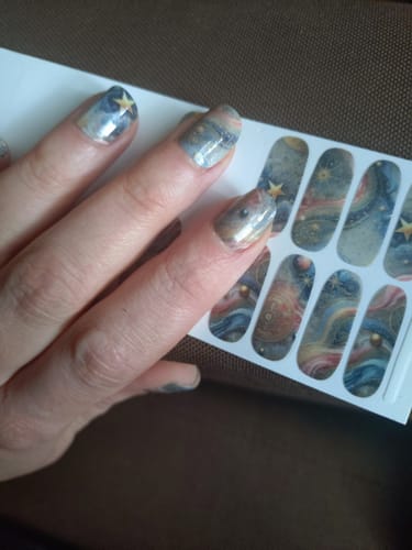 Kundenhand mit aufgetragenen, galaktischen Storybook Dreams Nagelfolien. Der unbenutzte Bogen liegt daneben.
