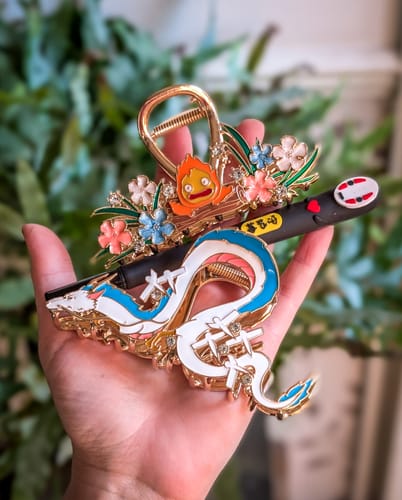 Reviewer holding several ornate Studio Ghibli hair claws, including the Haku dragon and Calcifer designs.