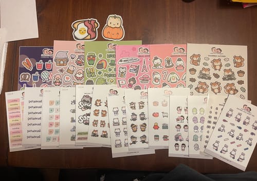 Customer's large assortment of sticker sheets from the Oopsie Mystery Bag spread out on a table.