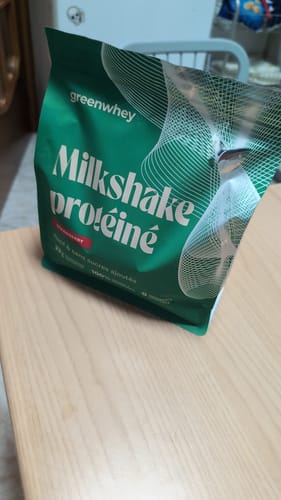 Sachet vert de Milkshake protéiné saveur fraise d'un client, posé sur une table.