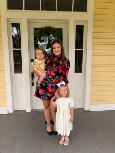 A reviewer's child wearing the Gold Surfer Sandals with a white dress on a porch.