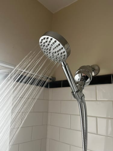 Customer's chrome Handheld Shower Head Set spraying a strong stream of water in a tiled shower.