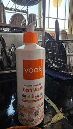 Customer's bottle of Dishwash Liquid with an orange pump, placed on a kitchen counter next to a dish rack.