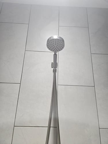 Customer's handheld shower head mounted in its holder against a modern tiled wall.