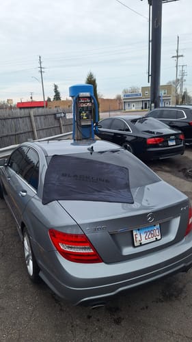 Customer's black BLACKLINE drying towel spread across the rear window of a grey car at a car wash.