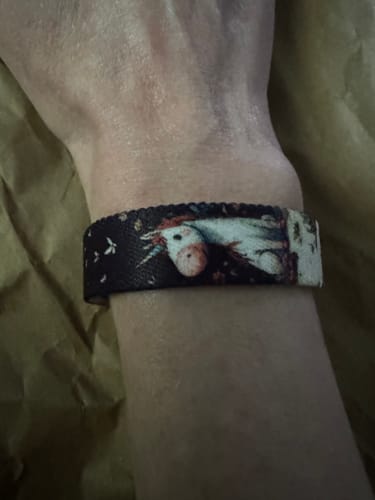 Reviewer wearing the dark Whimsy Bracelet with its whimsical unicorn graphic on their wrist.
