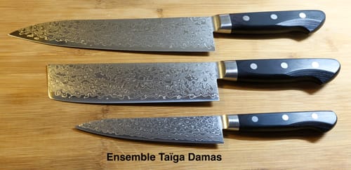 Reviewer's Taiga Damascus Starter Trio of three knives with patterned blades laid out on a wooden surface.