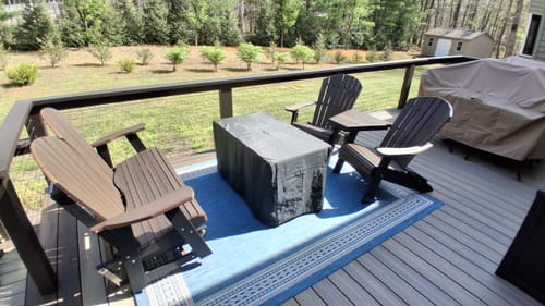 Customer's three brown Folding Adirondack Chairs arranged on a spacious wooden deck with a blue rug.