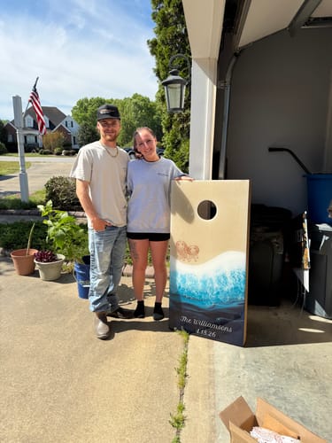 Customers holding a cornhole board with the reviewer's applied vinyl decal showing their name and wedding date.