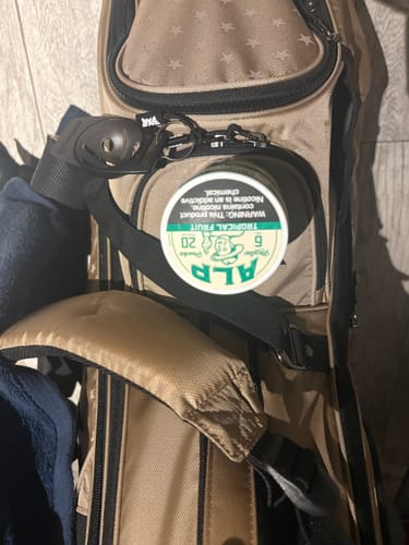 Customer's tin of Tropical Fruit Nicotine Pouches resting on the pocket of a tan golf bag.