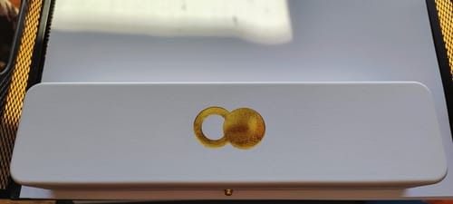 Packaging for The Empty Tomb necklace, showing the white box with the gold tomb and stone logo on top.