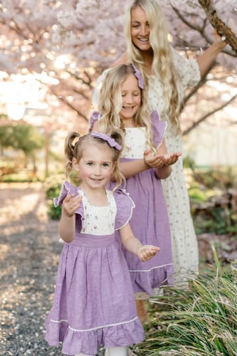 Customer's two children smiling in matching lavender linen Flutter Dresses outdoors.
