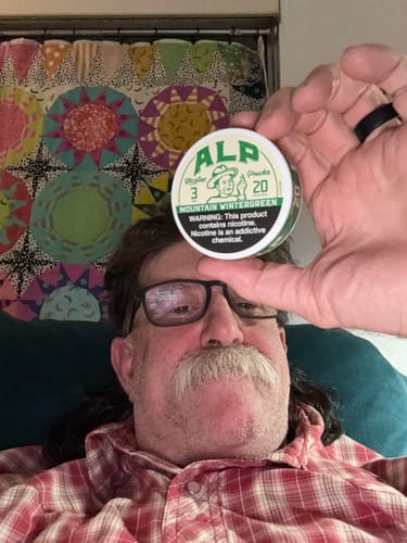 Reviewer holding a tin of ALP Mountain Wintergreen Nicotine Pouches in front of their face.