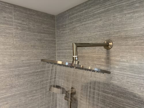 Customer's large 12 Inch Rain Shower Head installed and spraying water in a grey tiled shower.
