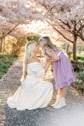 Reviewer kneels in the white floral Spring Florals Dress, looking up at a child under blossoming trees.