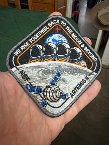 Customer holding the detailed Artemis II - Collectors Patch, showing astronauts above the Moon.