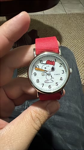 Un cliente sostiene el reloj Timex Snoopy, que tiene una correa roja y a Snoopy jugando béisbol en la esfera.